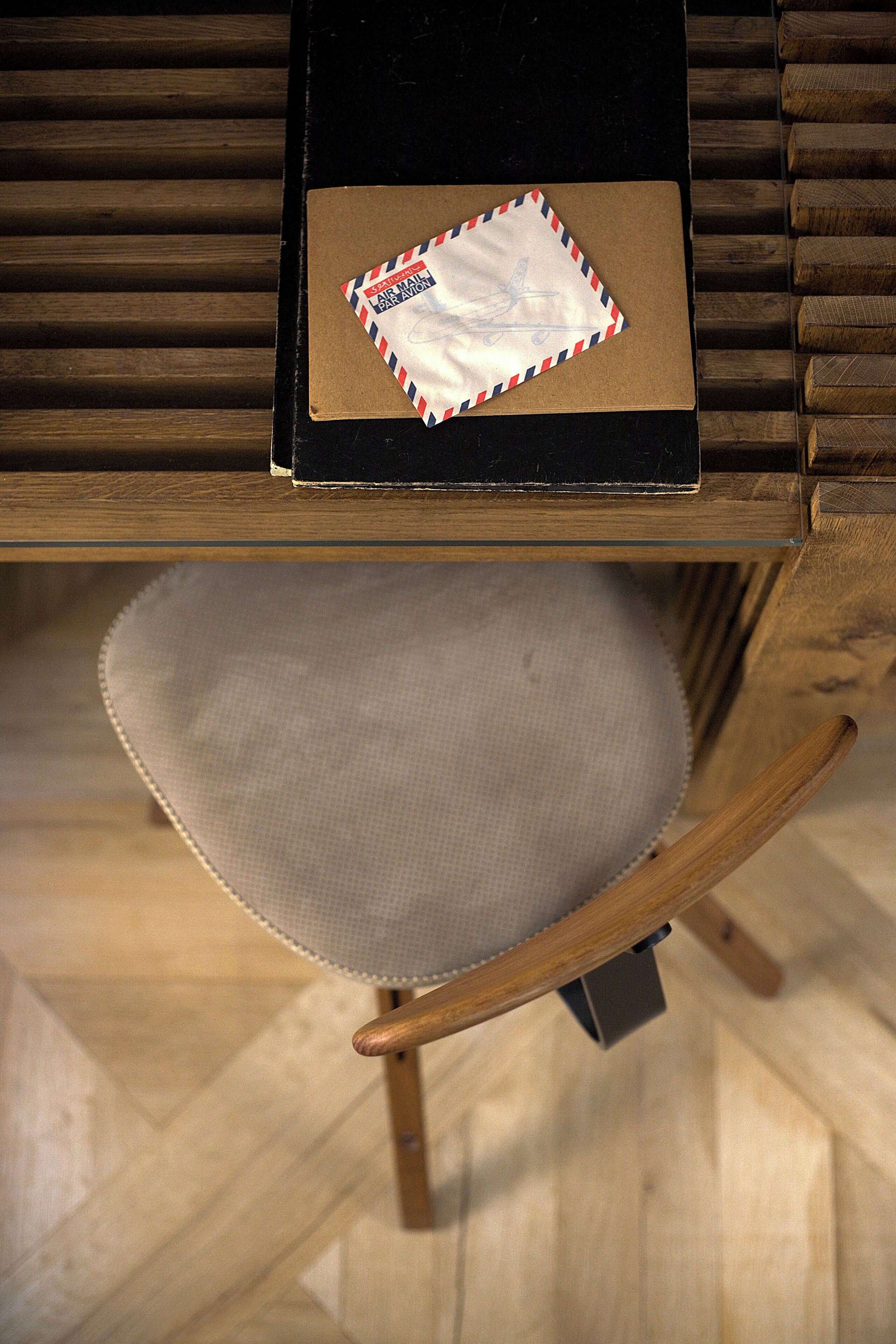 Una silla de madera con asiento acolchado y un sobre pequeño en el respaldo.