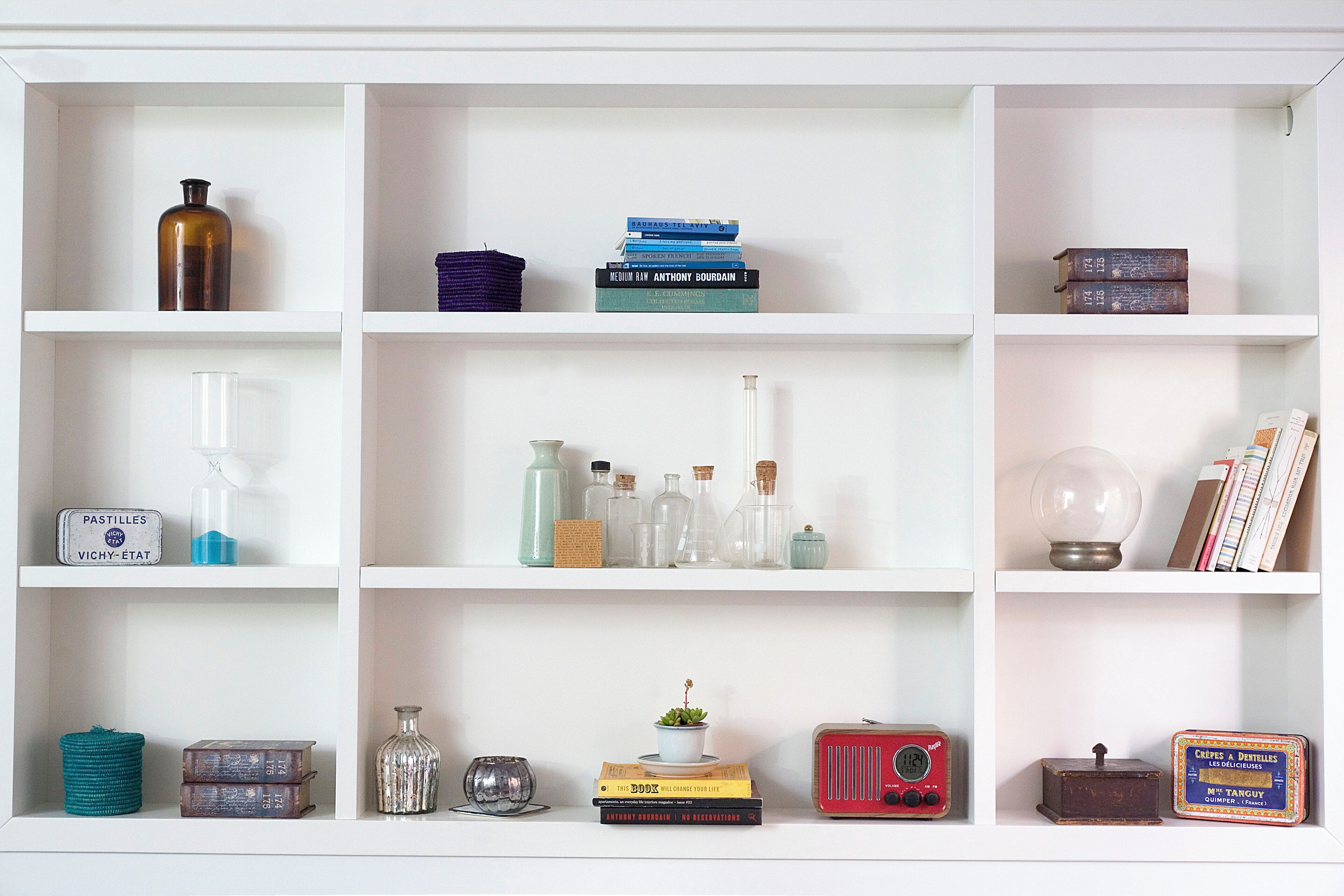 Une étagère blanche sur laquelle se trouvent divers objets, notamment des livres, des bouteilles et une radio.