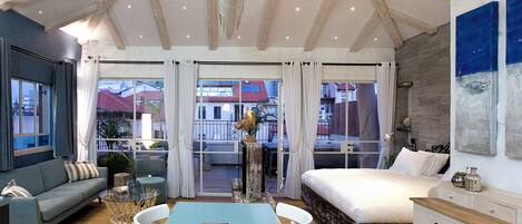 A spacious room with a large bed, a sofa, a dining table, and a view of the outside.