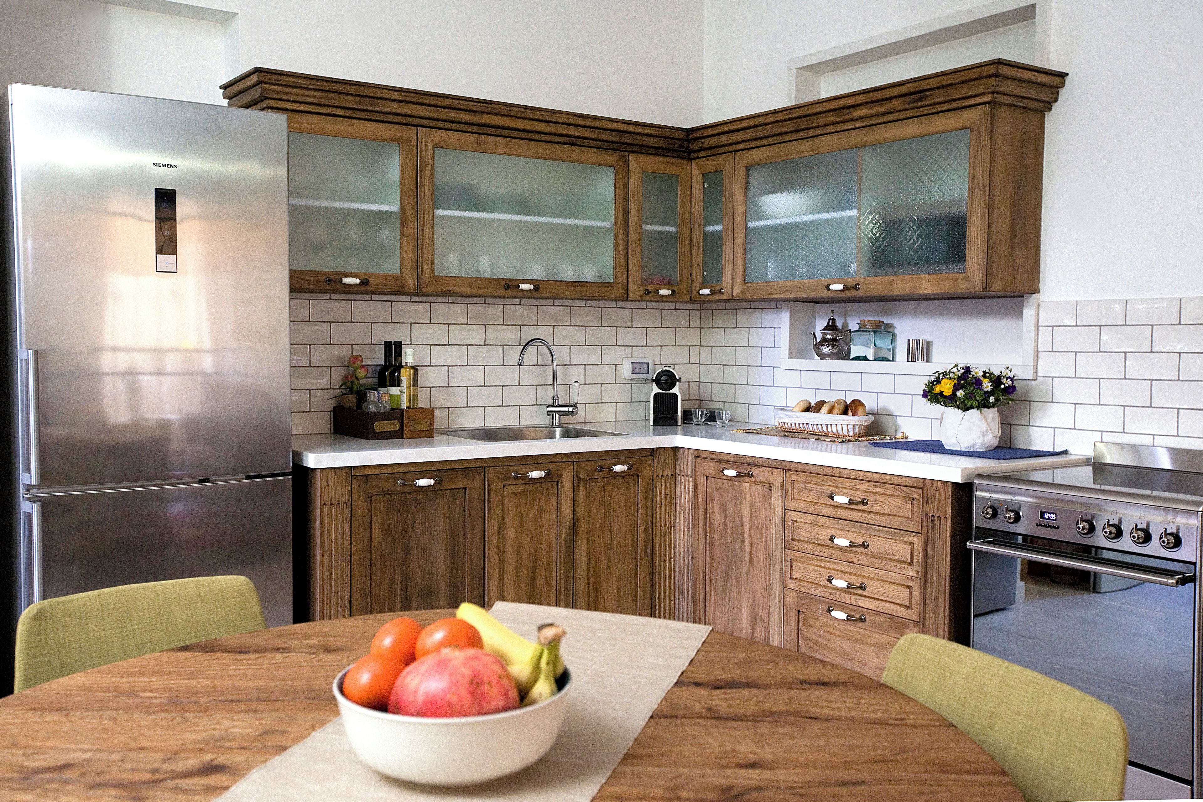 A kitchen with wooden cabinets, a stainless steel refrigerator, a stove, and a bowl of fruit on the table.