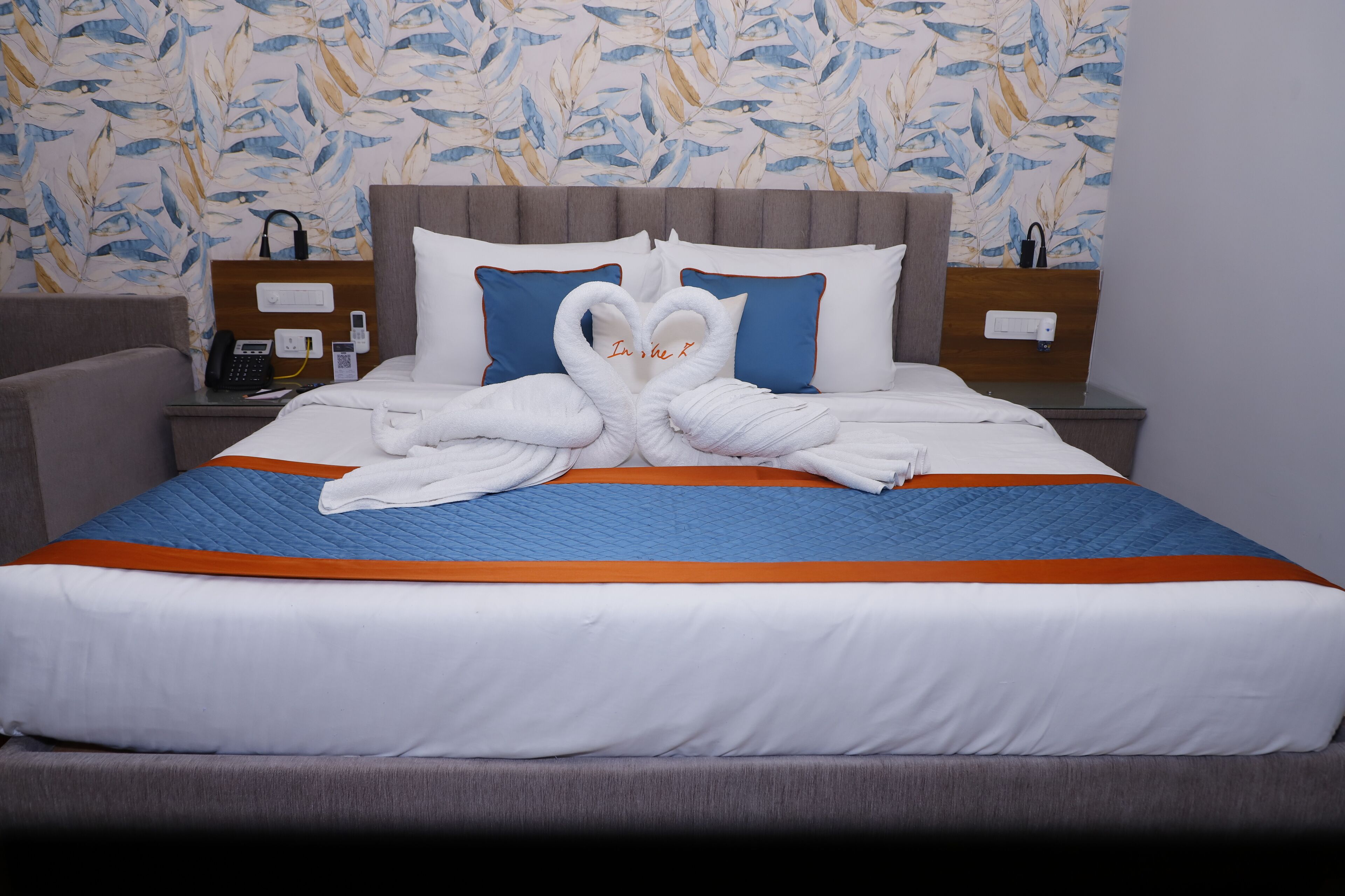 Habitación de hotel con cama, mesita de noche, teléfono y una pared con estampado de hojas.
