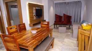 Un comedor con una mesa y sillas de madera, un banco, un televisor montado en un panel de madera y un sofá con sillas rojas.