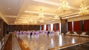 Un salón amplio con filas de mesas y sillas, candelabros decorados y un suelo con diseño.