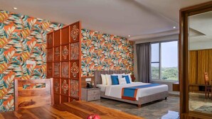 Habitación de hotel con cama, una mesa de madera con fruta, un muro decorativo y vistas al exterior.