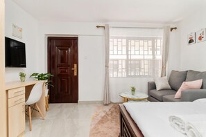 Un dormitorio moderno con cama, escritorio, televisor y ventana con cortinas.