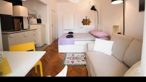 A compact living space with a kitchenette, a bed with a headboard, a sofa, and a chandelier. - Luxury living studio apartment with balcony in Split near center (Split)