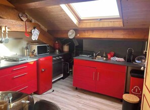 A compact kitchen with red cabinets, a microwave, a stove, and a skylight.