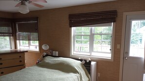 A bedroom with a bed, dresser, and a ceiling fan. There are windows with blinds and a door.