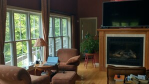 A spacious living room with a fireplace, large windows, and a television.