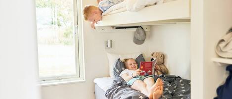 Una cama litera con un niño leyendo un libro y otro niño durmiendo en la parte superior.