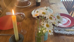 A wooden dining table with a candle, a bottle of wine, a cake, and a vase with flowers.