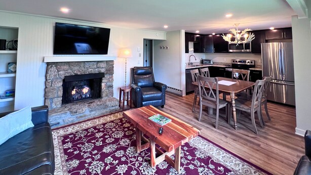 A living room with a fireplace, a TV mounted above it, a dining area with a table and chairs, and a kitchen with modern appliances. - Cozy Ski-Mountain Getaway (Sugar Mountain)