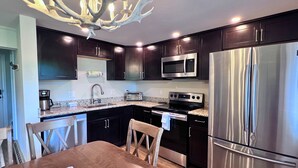 A modern kitchen with dark cabinets, stainless steel appliances, a granite countertop, and a dining area with wooden chairs and a table. - Cozy Ski-Mountain Getaway (Sugar Mountain)