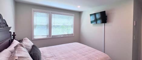A bedroom with a bed, a television mounted on the wall, and a window with blinds.