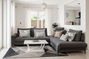 Una sala moderna con un sofá modular gris, una mesa de centro blanca y una alfombra estampada.