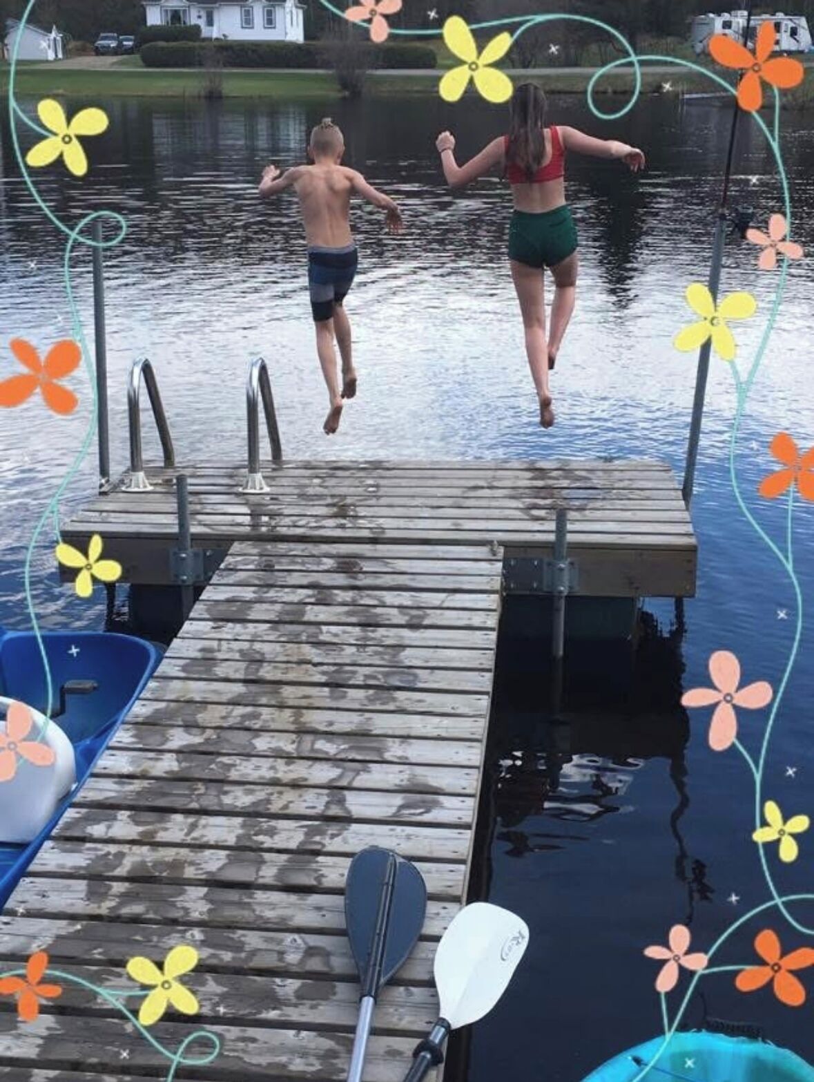 En træbrygge der strækker sig ud i vandet, med en robåd og en stand-up paddleboard i nærheden.