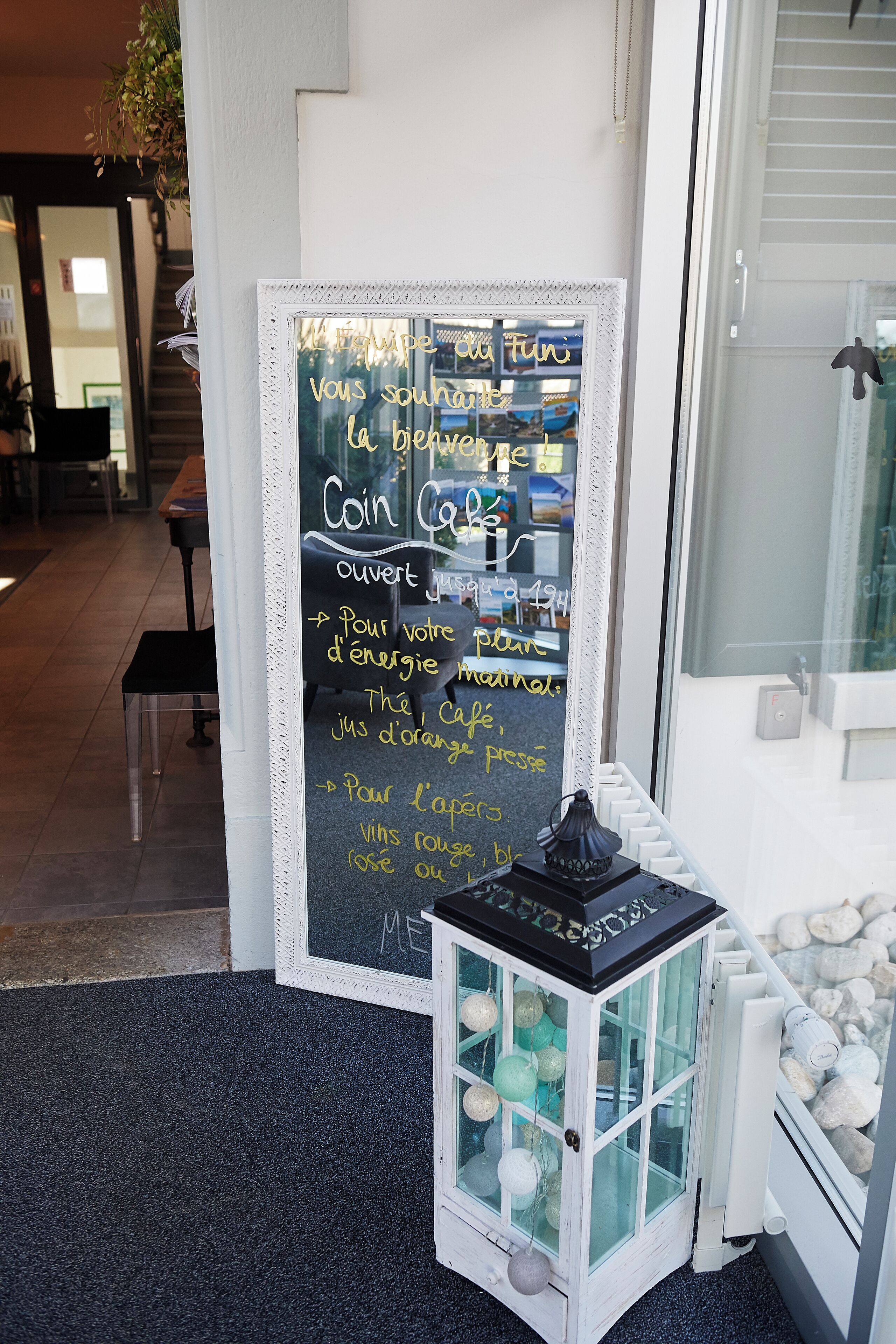 A chalkboard sign with French text, a small lantern, and a window with a view of the street.