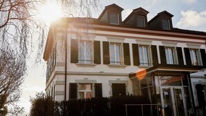 Un bâtiment à deux étages doté d’une façade symétrique, de grandes fenêtres avec volets et d’une entrée centrale bien visible.