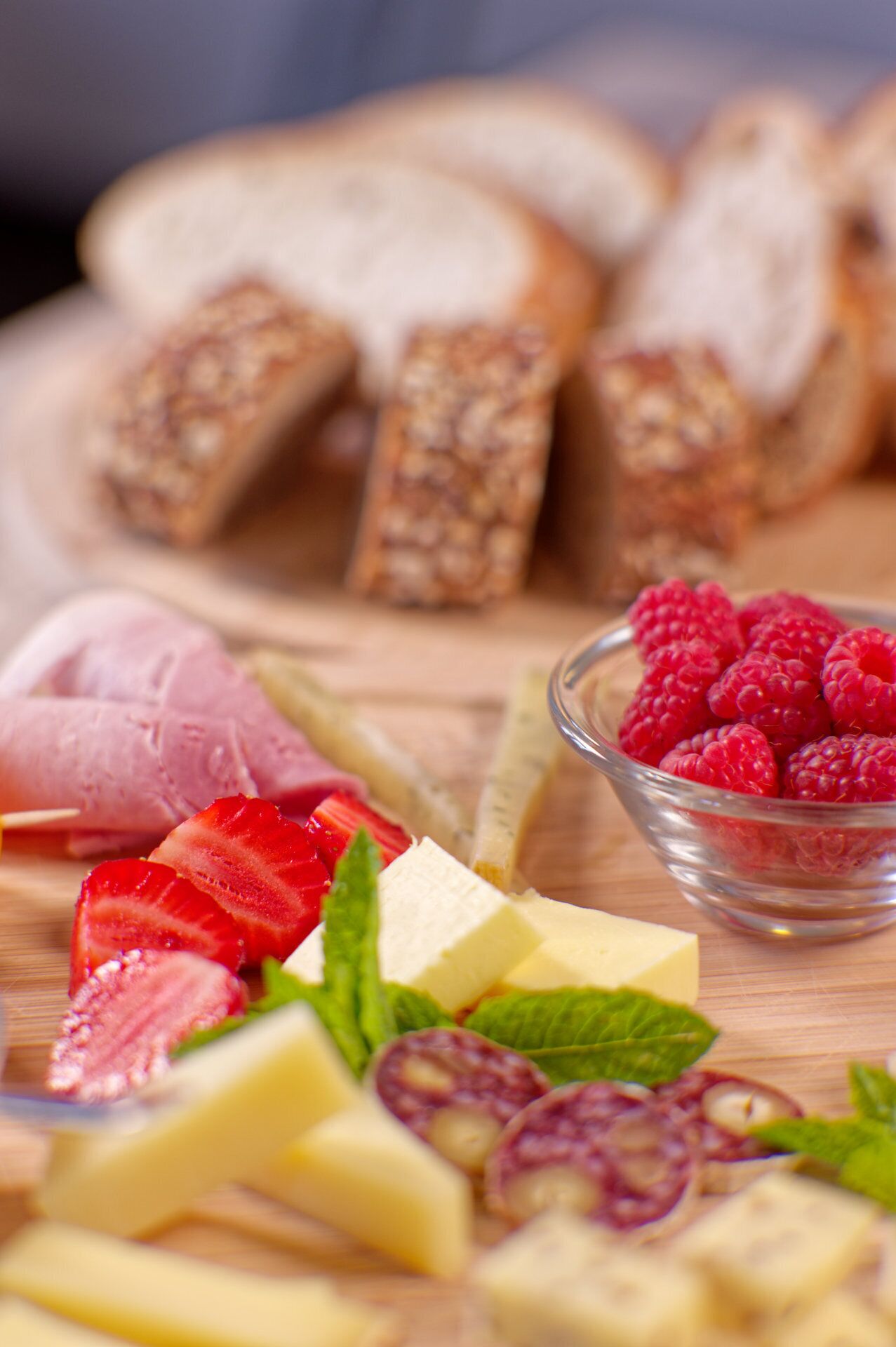 Un assortimento di formaggi, frutta e pane su un tagliere di legno.
