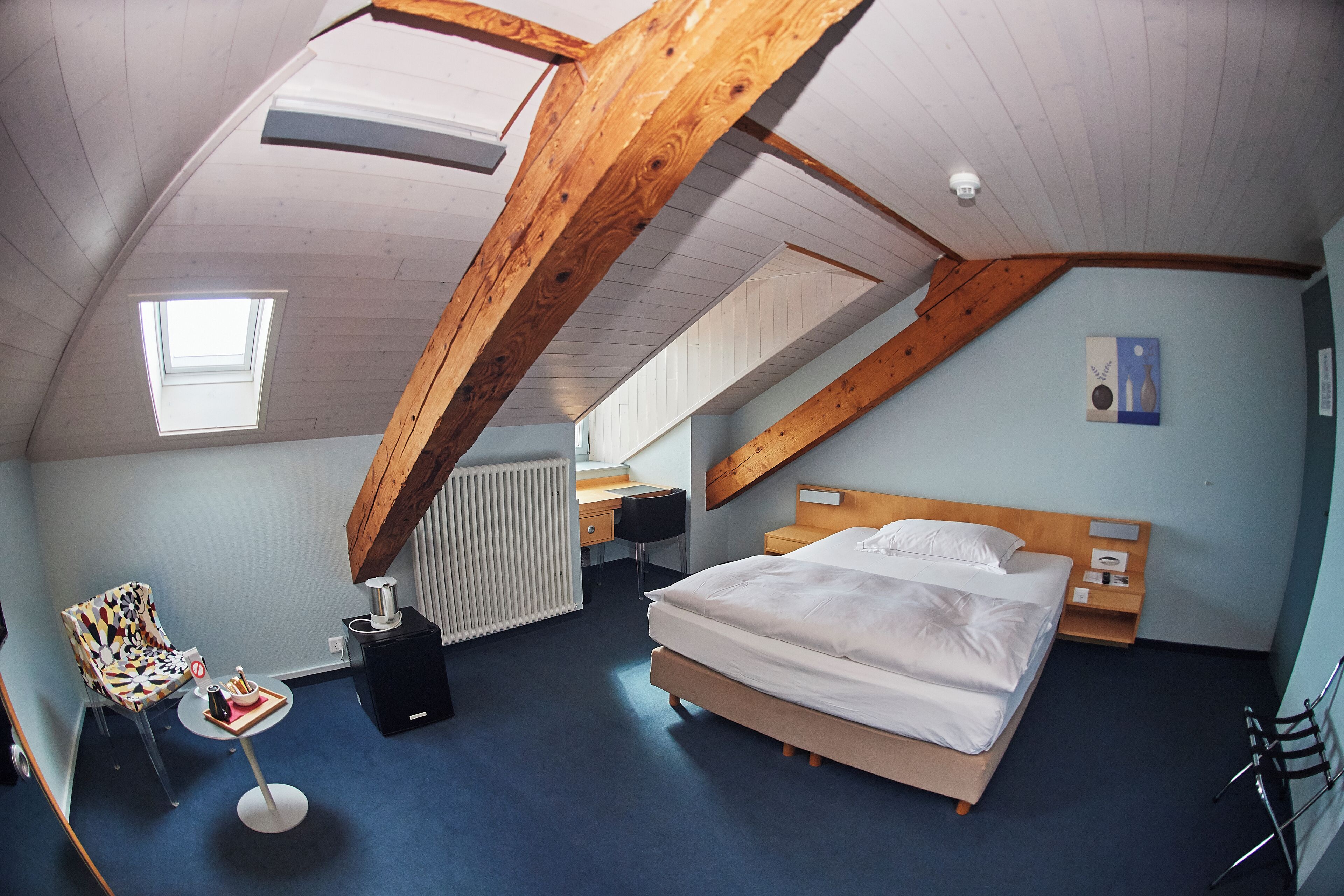 A bedroom with a sloped ceiling, a bed, a desk, a chair, and a radiator.