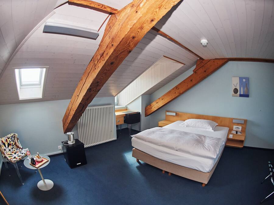 A bedroom with a sloped ceiling, a bed, a desk, a chair, and a radiator.