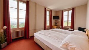Une chambre d’hôtel avec deux lits, une télévision, une petite table avec un vase et une vue sur l’extérieur.
