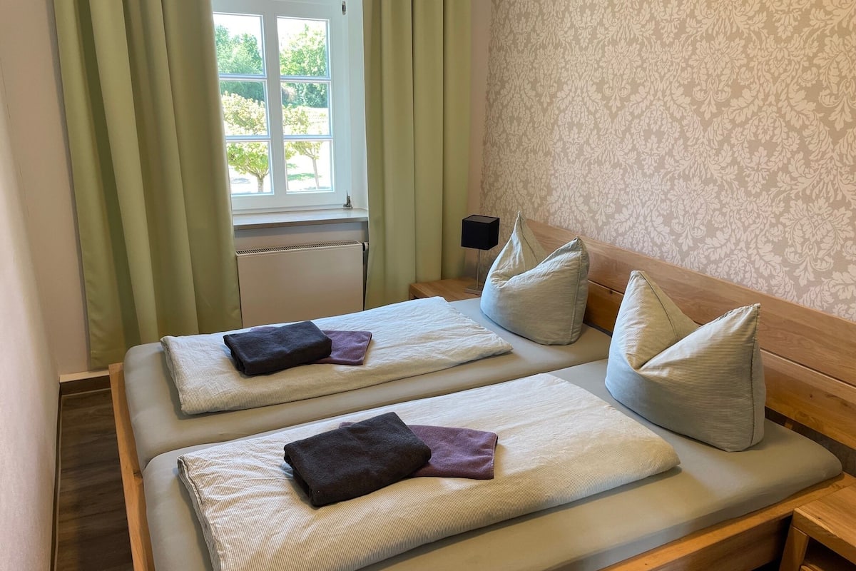 A double bed with two pillows, a bedside table, and a window with curtains.