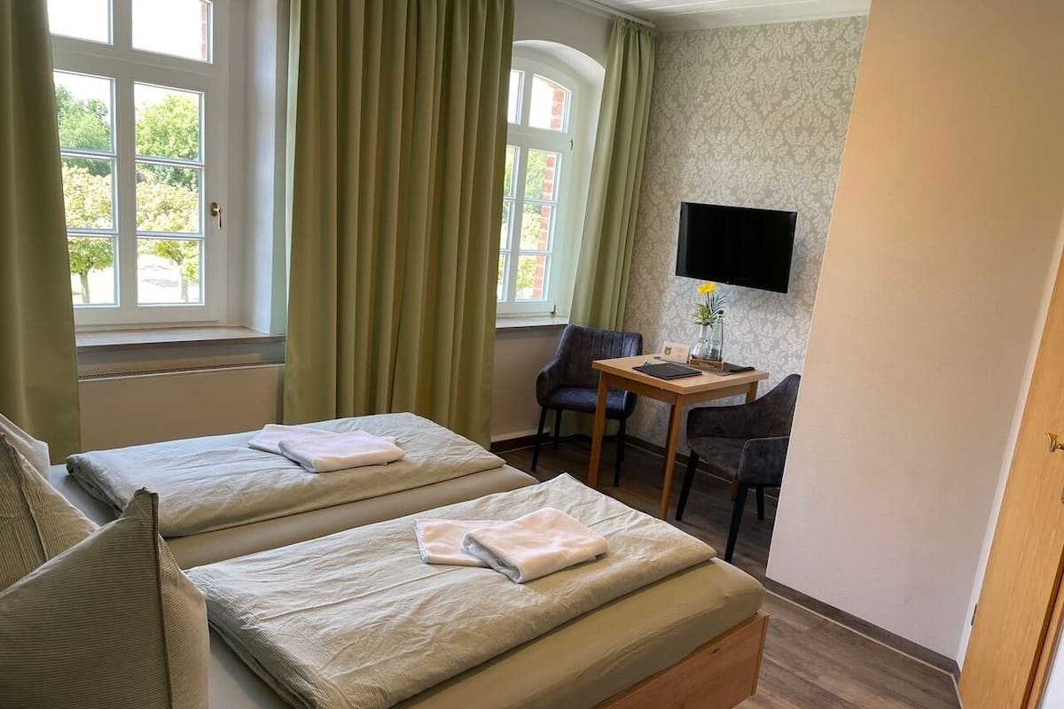 A hotel room with two beds, a desk, a chair, a TV, and a window with curtains.