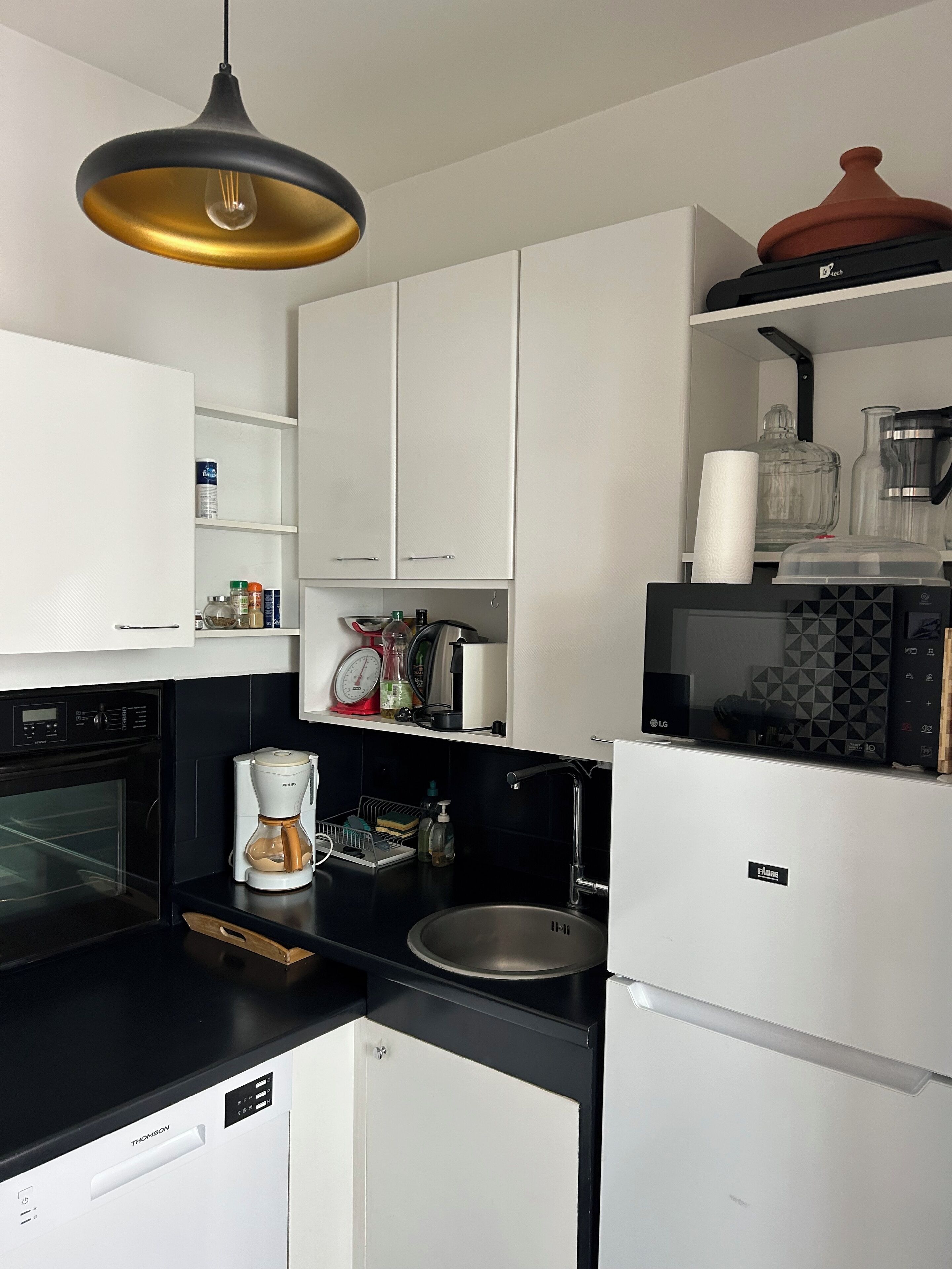 A modern kitchen with white cabinets, a black countertop, a coffee maker, a kettle, and a refrigerator.