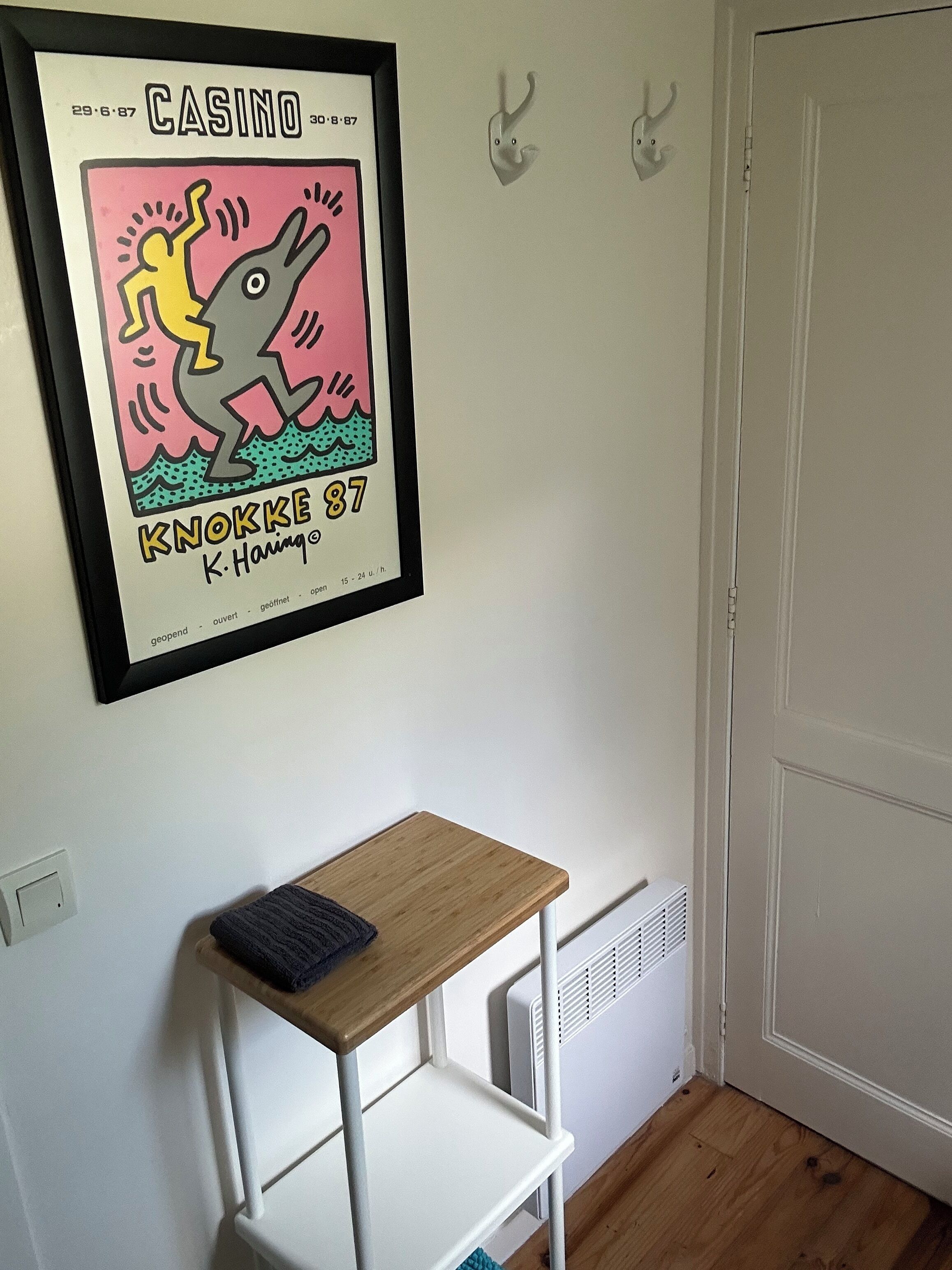 A framed artwork of a cartoon character on a wall, a small wooden table, and a white radiator.