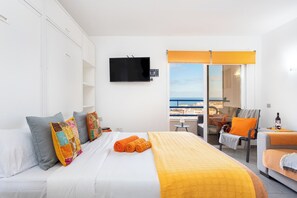 A hotel room with a bed, a TV, a balcony with a view, and a seating area.