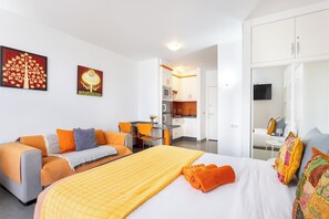 A hotel room with a bed, a sofa, a dining table, and a kitchen area.