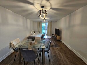 Ett modernt vardagsrum med ett glasbord, två stolar, en soffa, en tv och ett stort fönster med gardiner.