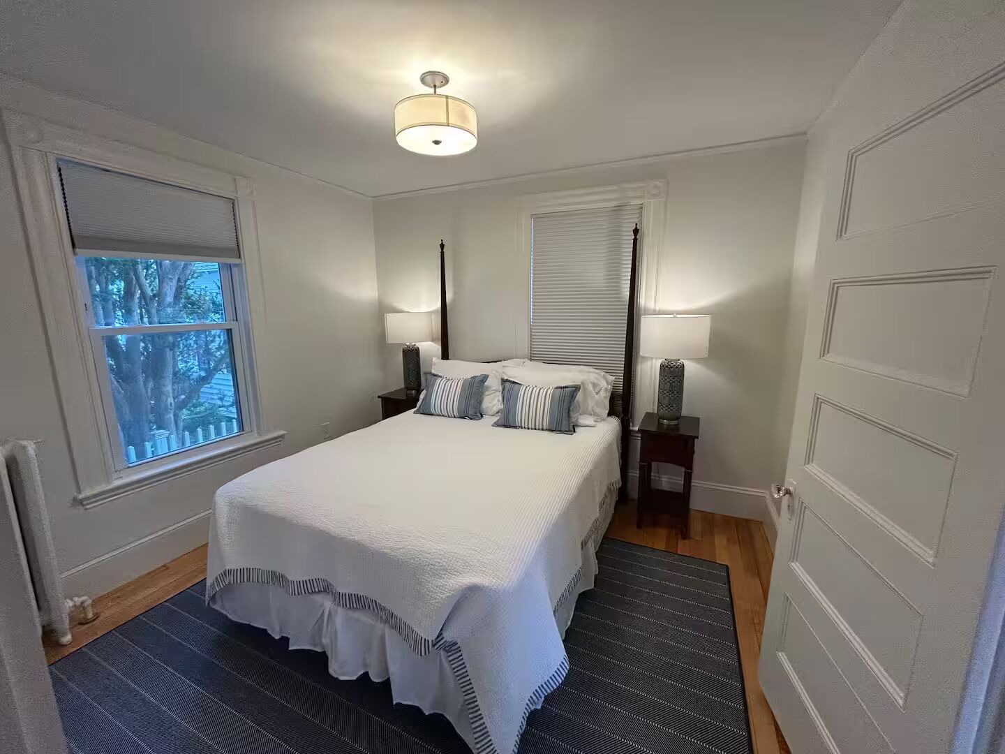 Un dormitorio con una cama, dos mesitas de noche, una ventana y una puerta.