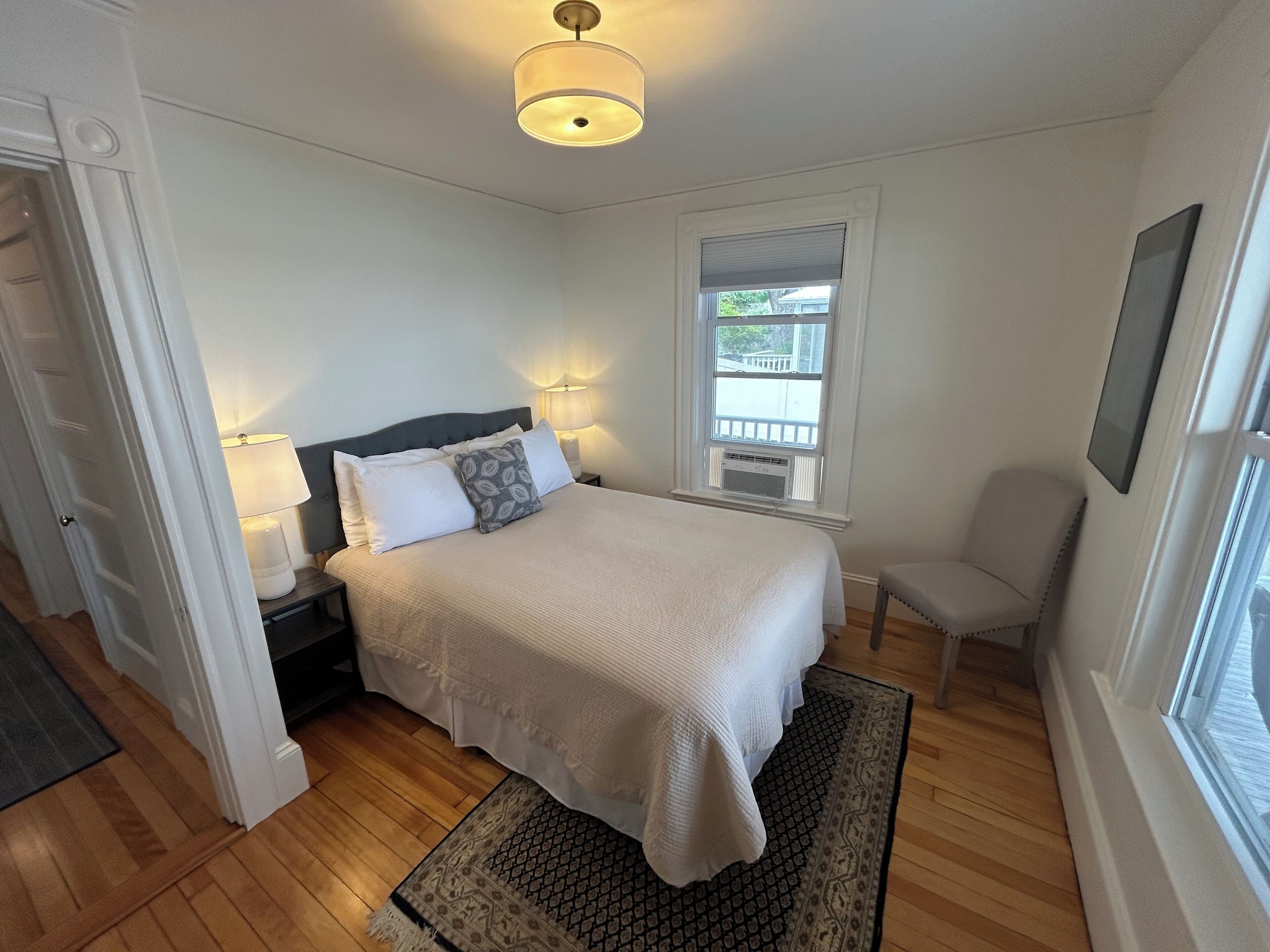 A bedroom with a bed, bedside lamps, a window, a chair, and a door.