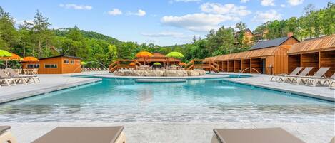 A swimming pool with lounge chairs and umbrellas, surrounded by wooden buildings and trees.