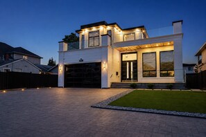 Une maison moderne à deux étages, dotée d’un garage, d’une allée bien éclairée et d’une petite pelouse.