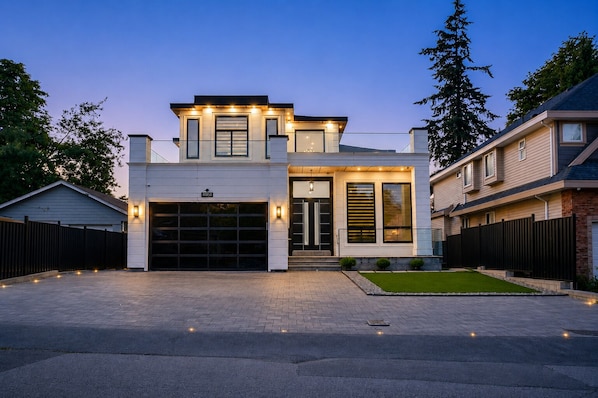 Une maison moderne à deux étages, dotée d’un garage, d’une entrée bien éclairée et d’un jardin aménagé.