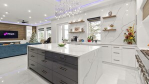 Une cuisine moderne avec un îlot en marbre, des meubles blancs et un lustre.