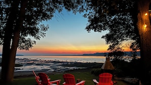 Three red Adirondack chairs facing a sunset over a beach with a view of the ocean and distant hills. - Magnificient view on the St-Lawrence river with private beach (Lévis)