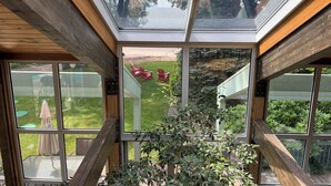 A modern house with a glass ceiling, wooden beams, and a view of a backyard with red chairs and greenery. - Magnificient view on the St-Lawrence river with private beach (Lévis)