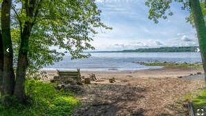 A beach with trees, a wooden bench, and a calm lake. - Magnificient view on the St-Lawrence river with private beach (Lévis)