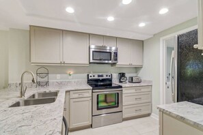 Una cocina moderna con electrodomésticos de acero inoxidable, encimeras de mármol y armarios blancos.