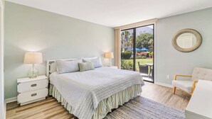 Une chambre à coucher avec un lit, des tables de chevet, une chaise et une vue sur l’extérieur.