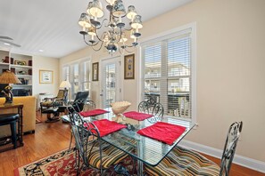 Un coin repas avec une table en verre, des chaises en métal, des sets de table rouges et un lustre.