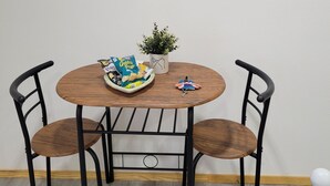 Una mesa redonda de madera con dos sillas de metal negro, una pequeña planta en maceta, un cuenco de aperitivos y un adorno lunar colgado en la pared.