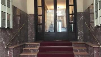 Eine Marmortreppe mit rotem Teppich, der zu einer dunklen Holztür mit Glasfenstern führt.