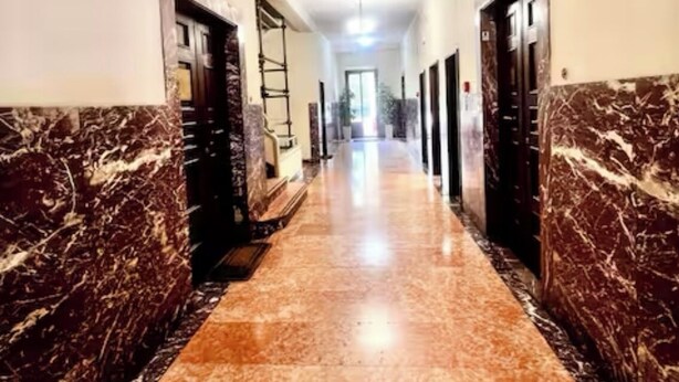 A long, narrow hallway with marble flooring and walls, leading to a bright room at the end. - Cozy Sweet Marbel room in the center of Florence (Firenze)