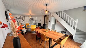 Een eetruimte met een houten tafel, gele stoelen en een vaas met decoratieve takken.