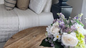 Un dormitorio con cama, almohadas, una mesita de noche, una lámpara y un florero con flores.